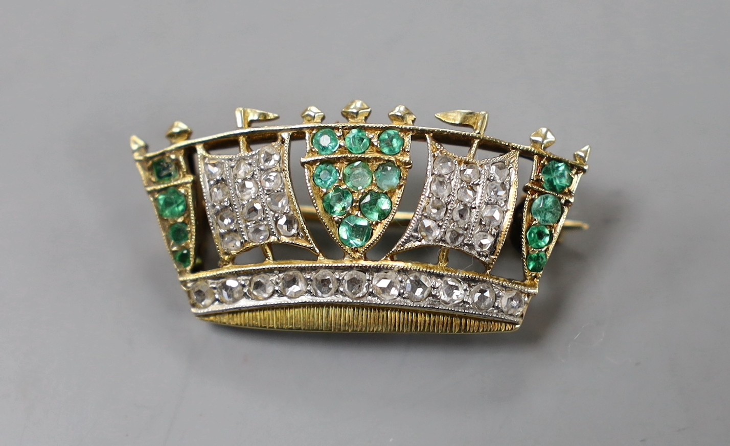 An early 20th century yellow metal, emerald and diamond set coronet brooch, 30mm, gross weight 4.4 grams.